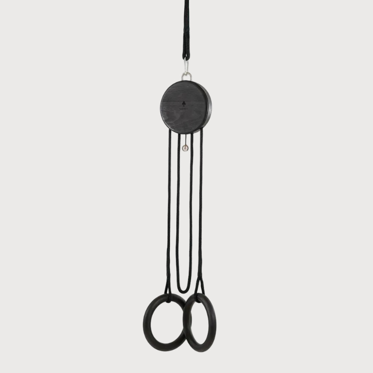 A minimalist black hanging weight set featuring a circular pulley wheel and two hanging rings, suspended against a solid light gray background.