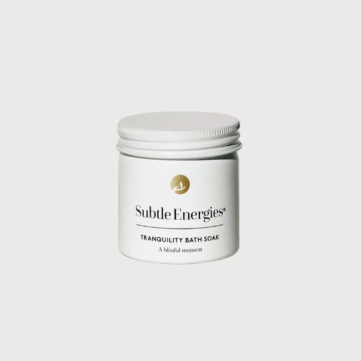 A white jar of Subtle Energies Tranquility Bath Soak with a white lid, set on a light beige textured surface against a white background.