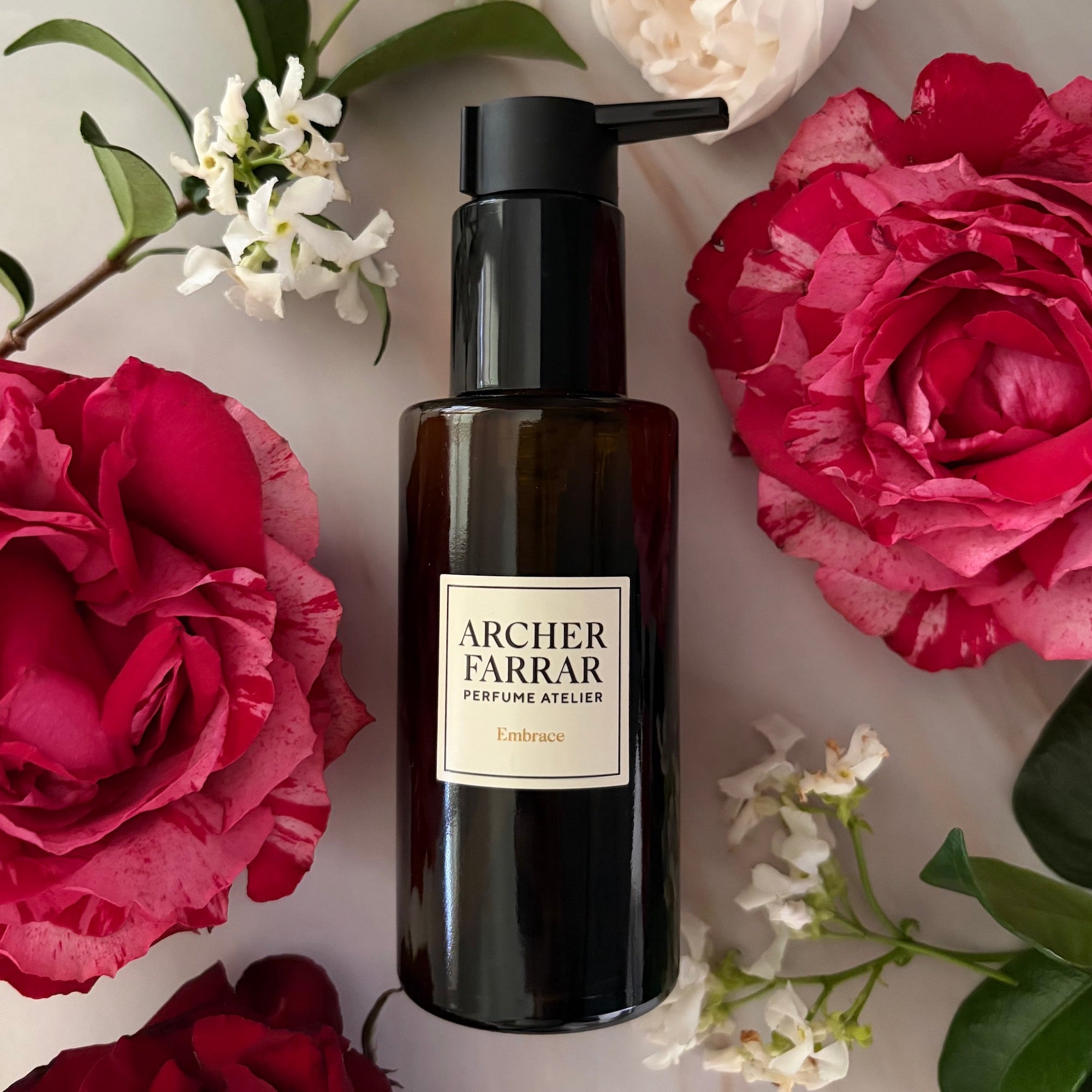 Black bottle with a label on a surface surrounded by red and white flowers