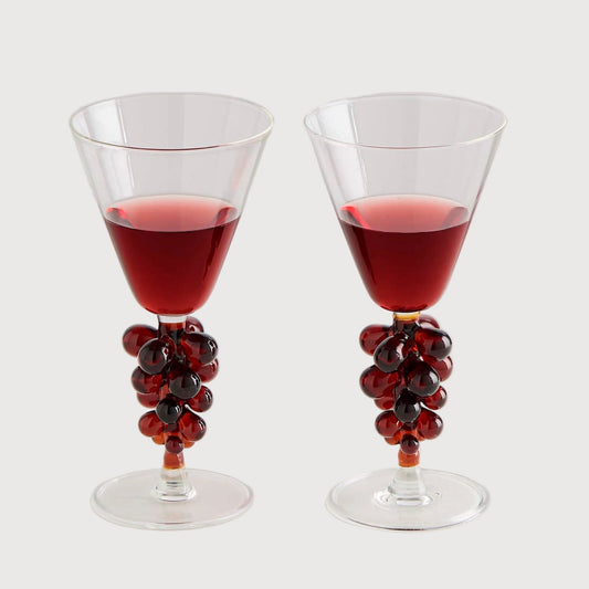 Two glasses with red liquid and decorative grapes on a white background
