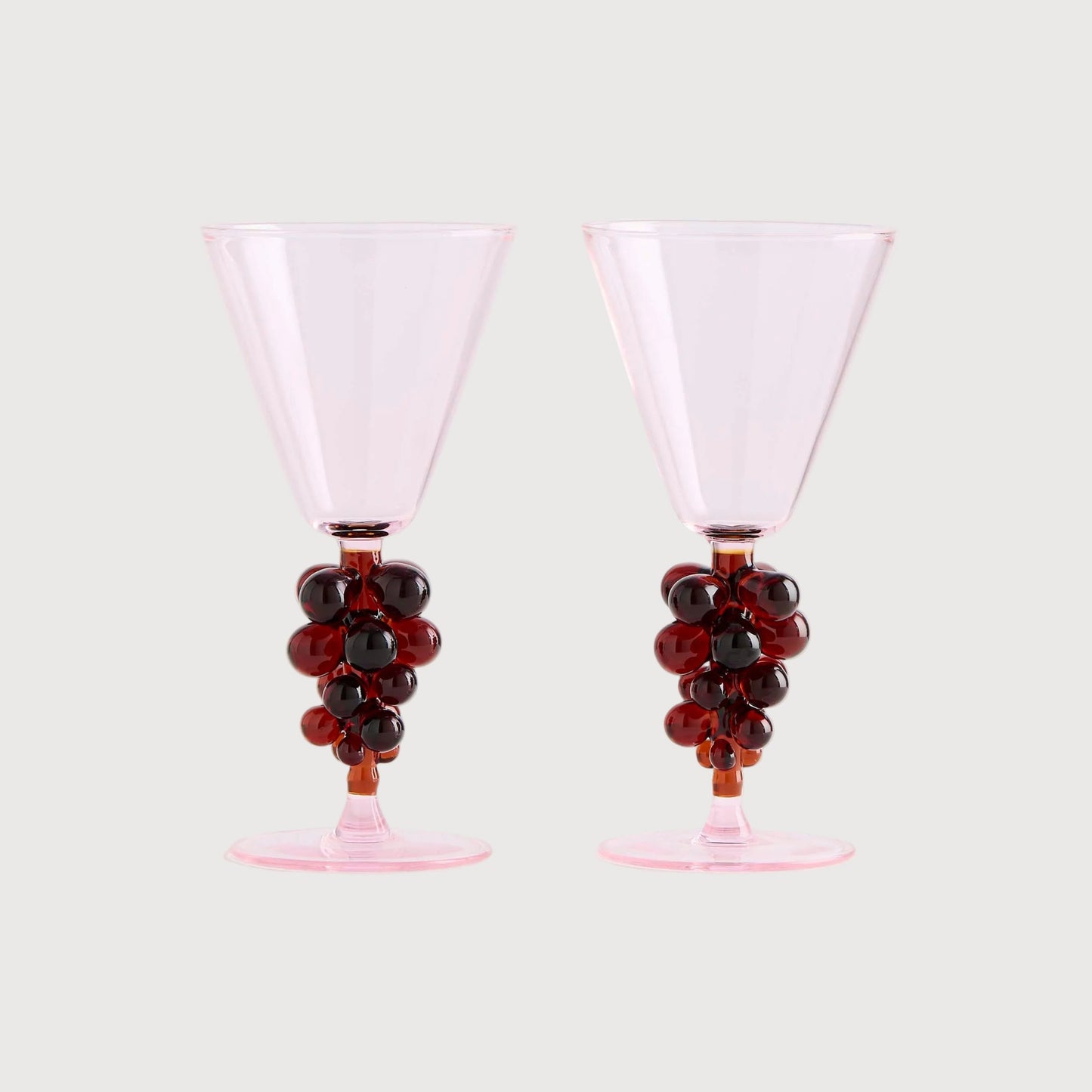 Two pink cocktail glasses with grape decorations on a white background