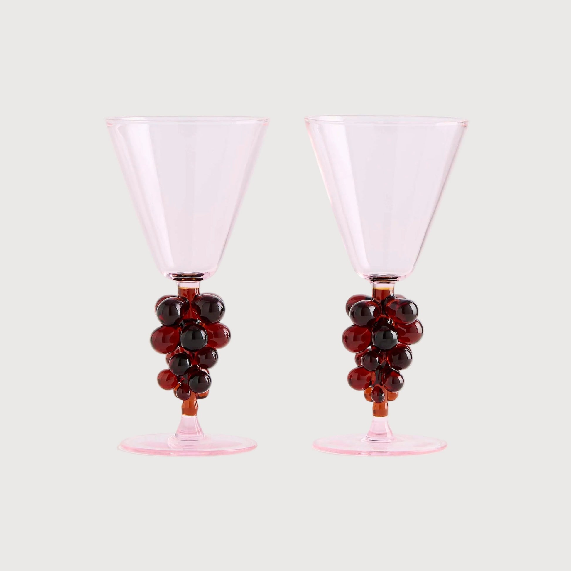 Two pink cocktail glasses with grape decorations on a white background