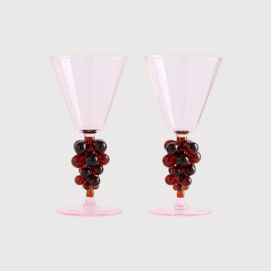 Two pink cocktail glasses with grape decorations on a white background