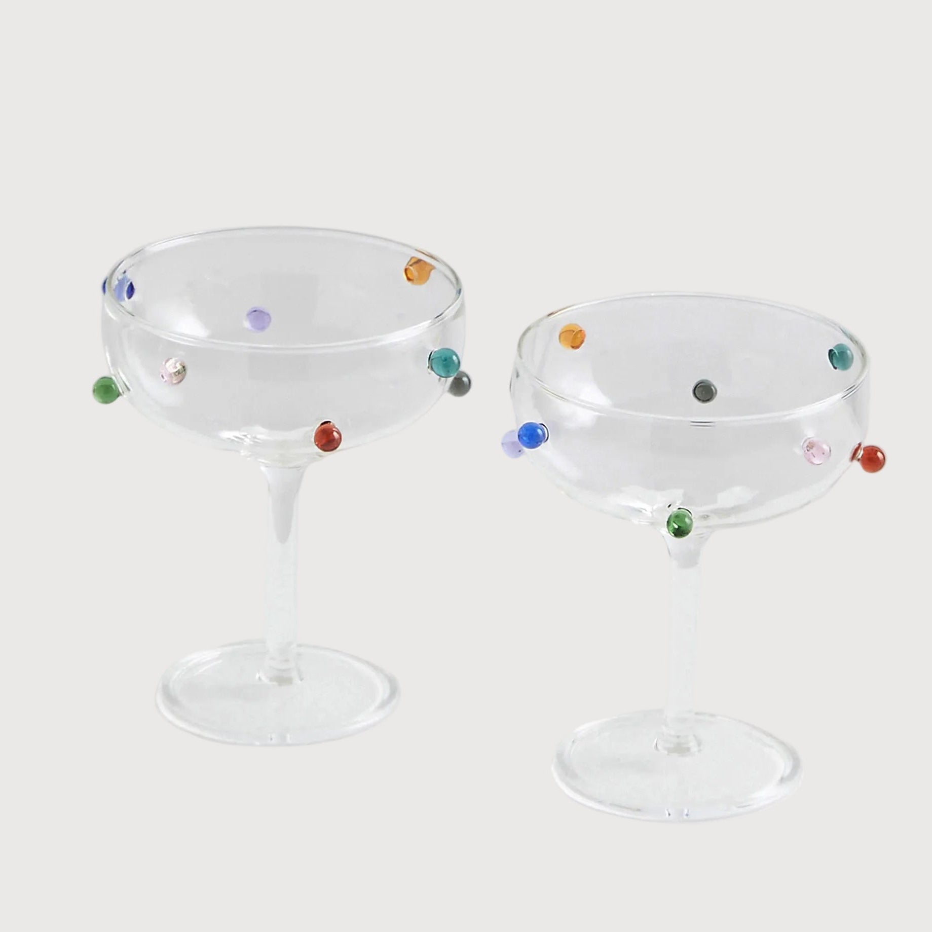 Two glass cocktail glasses with colorful dots on a white background
