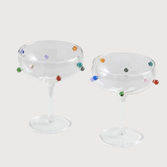 Two glass cocktail glasses with colorful dots on a white background