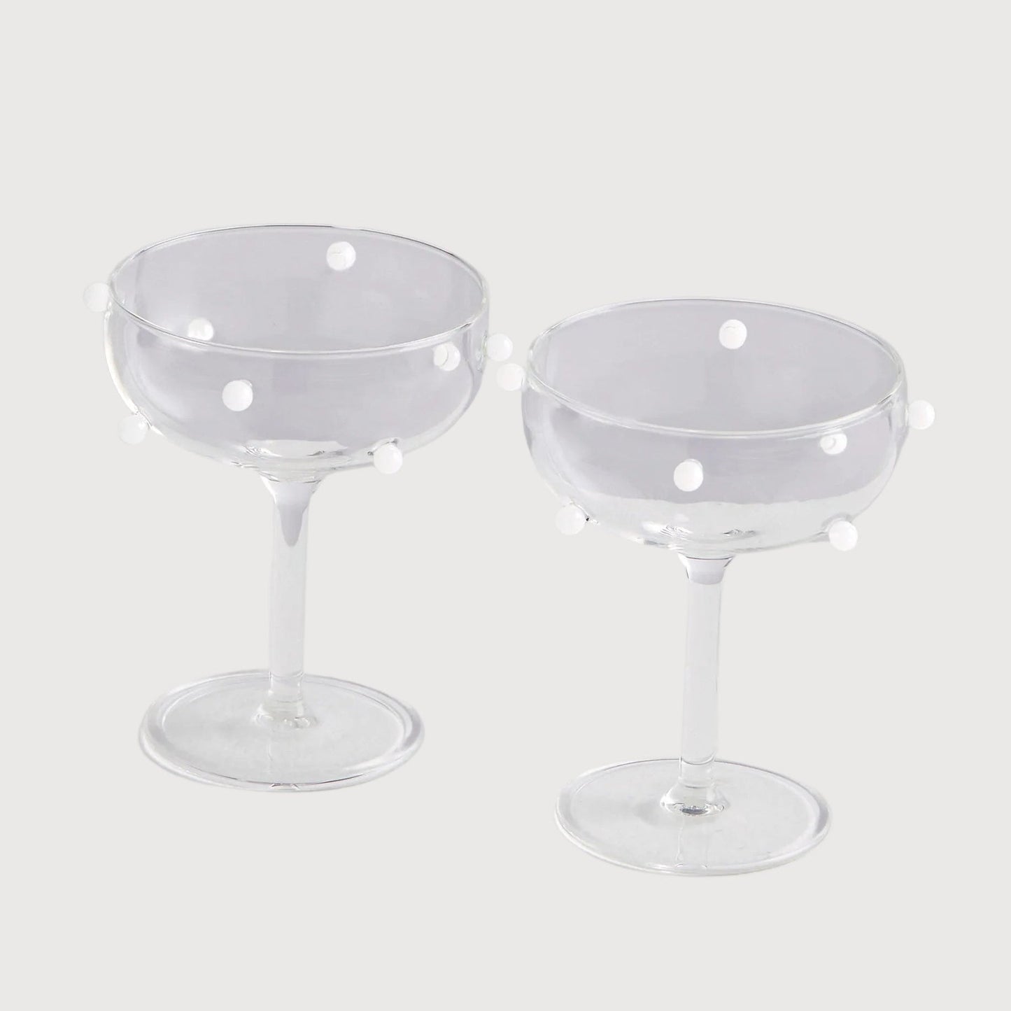 Two clear glass coupe glasses with small holes on a light gray background