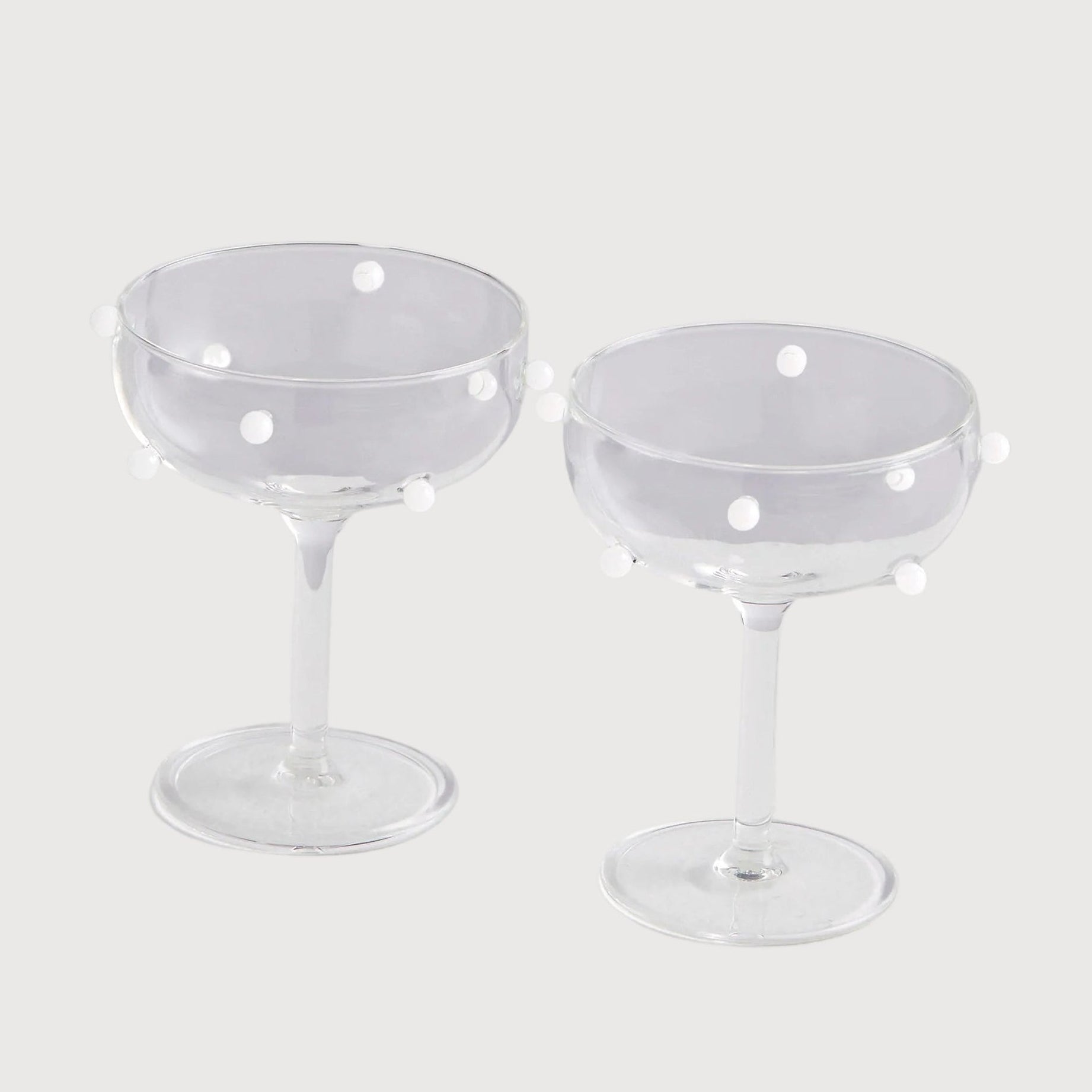 Two clear glass coupe glasses with small holes on a light gray background
