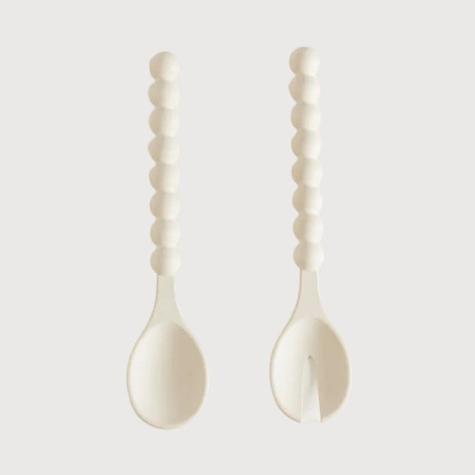 Two white ceramic spoons with textured handles on a light gray background