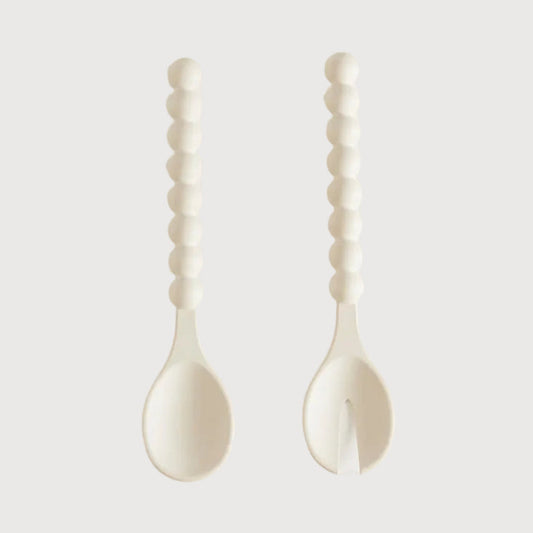 Two white ceramic spoons with textured handles on a light gray background