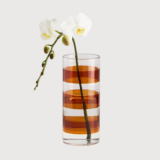 Tall glass with striped design containing a white orchid on a light gray background