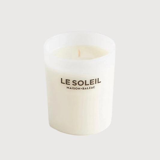 Small white candle with 'LE SOLEIL' branding on a light gray background