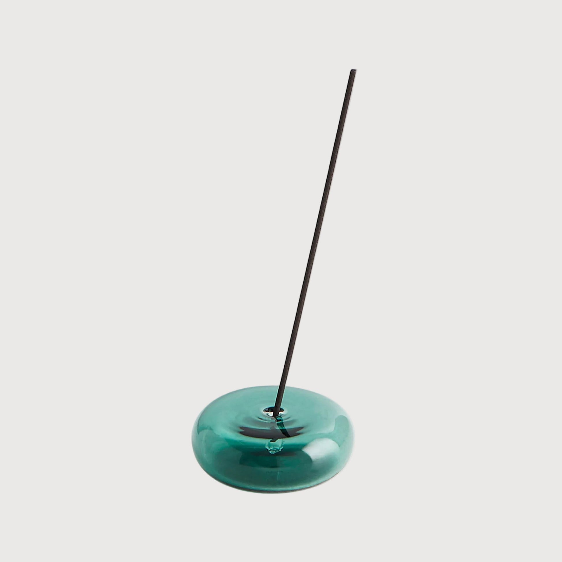 Teal incense holder with a single incense stick on a light gray background