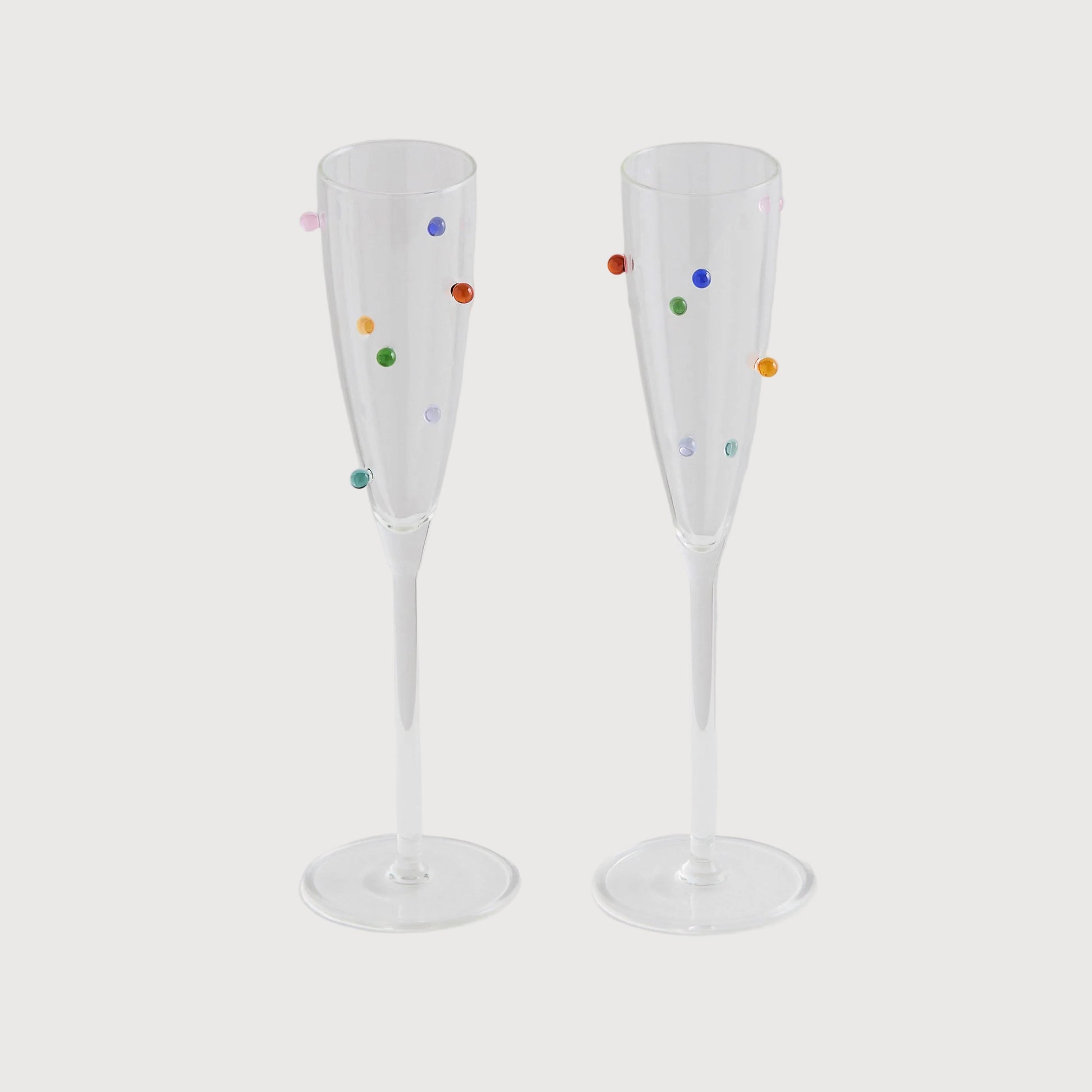 Two clear champagne flutes with colorful polka dots on a light gray background