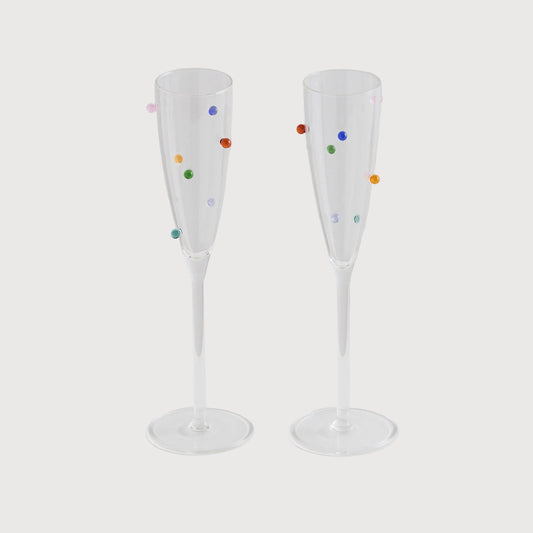 Two clear champagne flutes with colorful polka dots on a light gray background