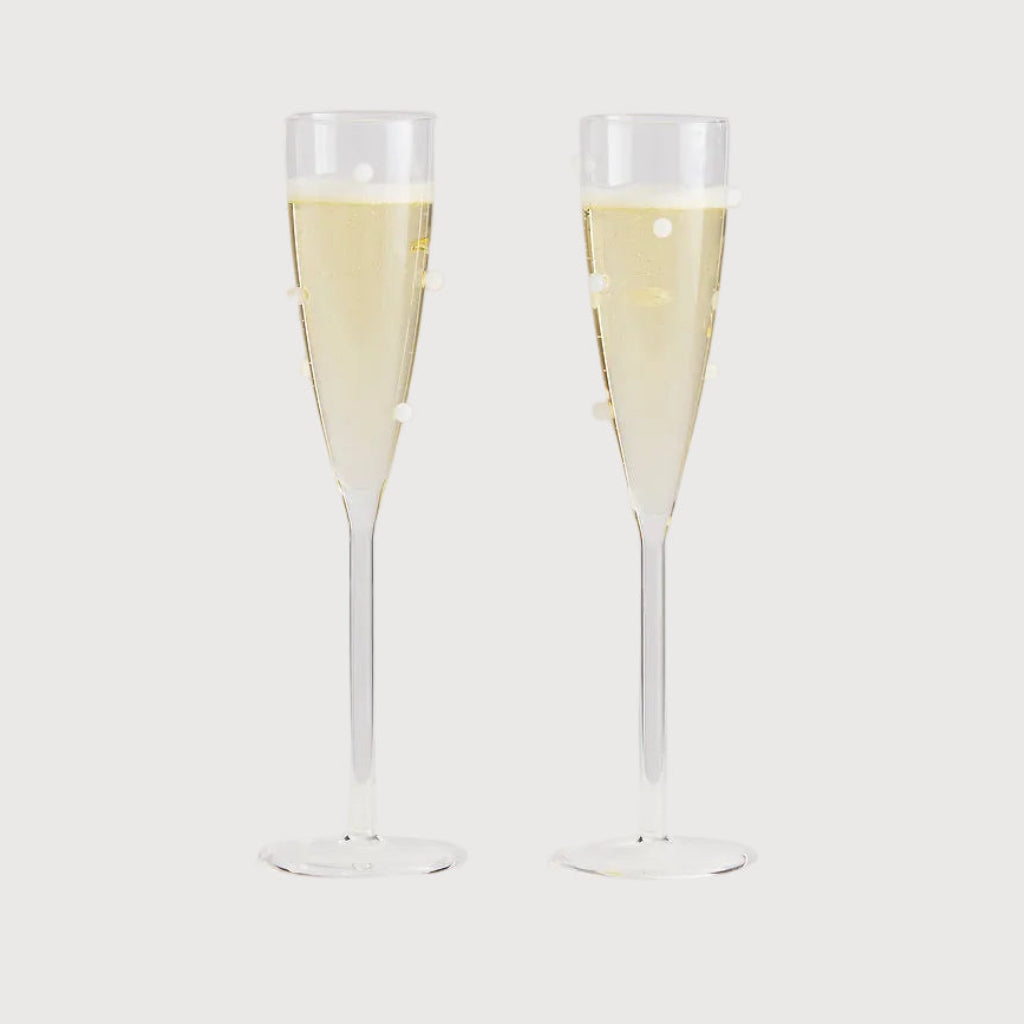 Two champagne flutes filled with champagne on a light gray background