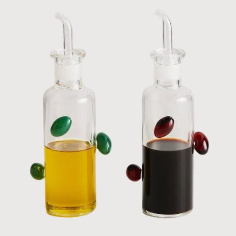 Two glass oil and vinegar bottles with olive and cherry designs on a white background