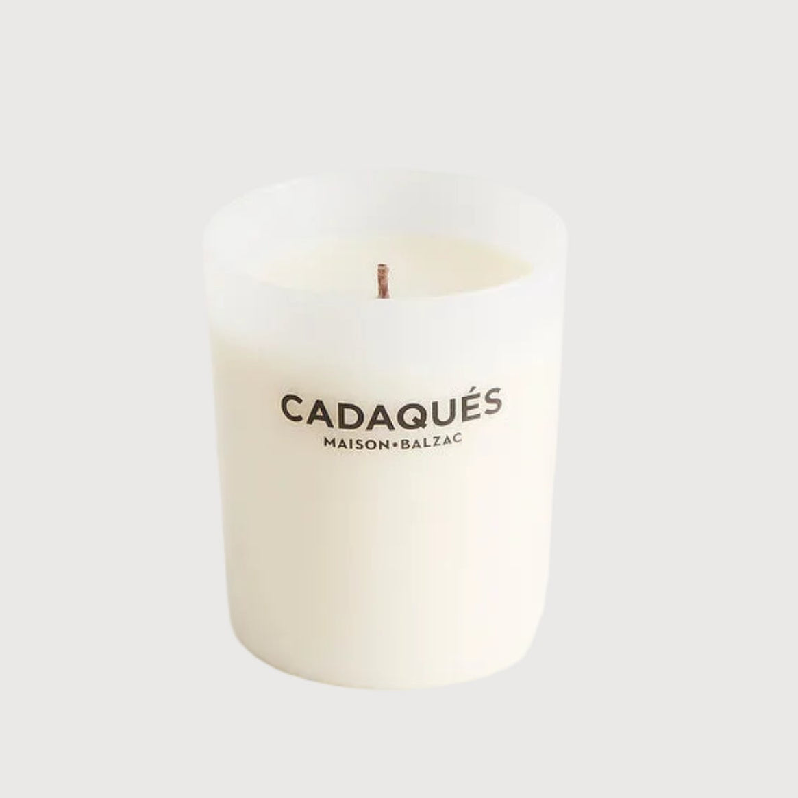 White candle with 'Cadaqués' branding on a light gray background