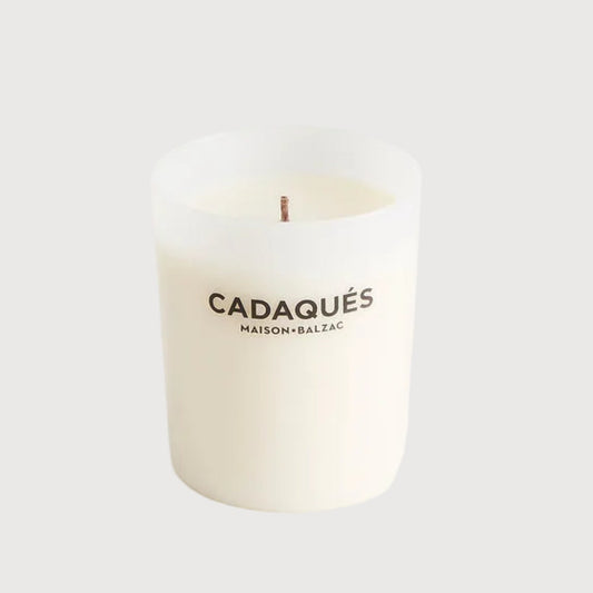 White candle with 'Cadaqués' branding on a light gray background