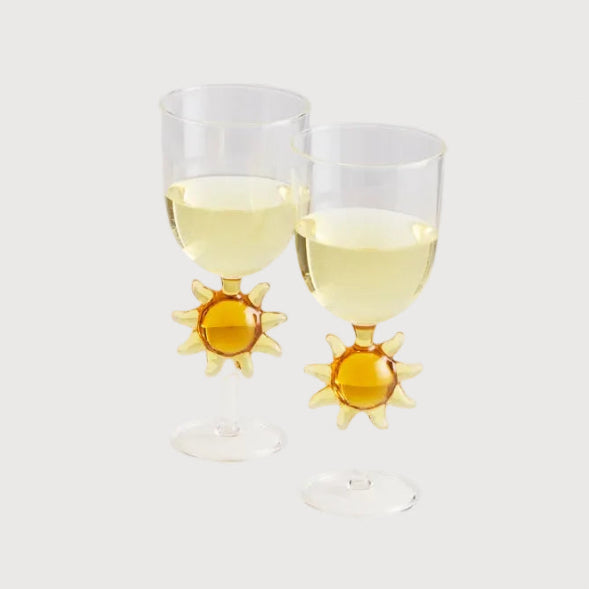 Two glasses with sun-shaped stems filled with a white liquid on a light gray background