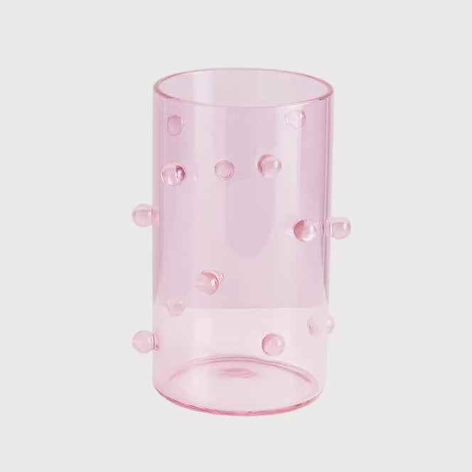 Pink glass tumbler with small knobs on a light pink background