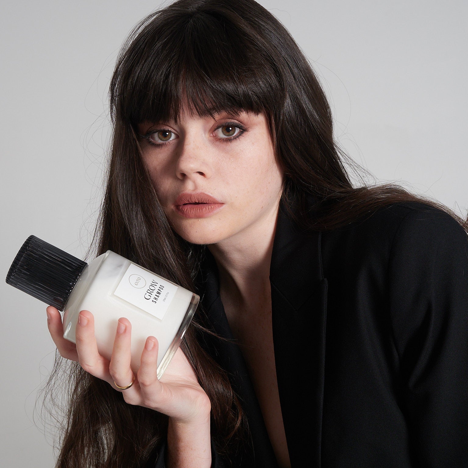 Woman holding a perfume bottle against a plain background