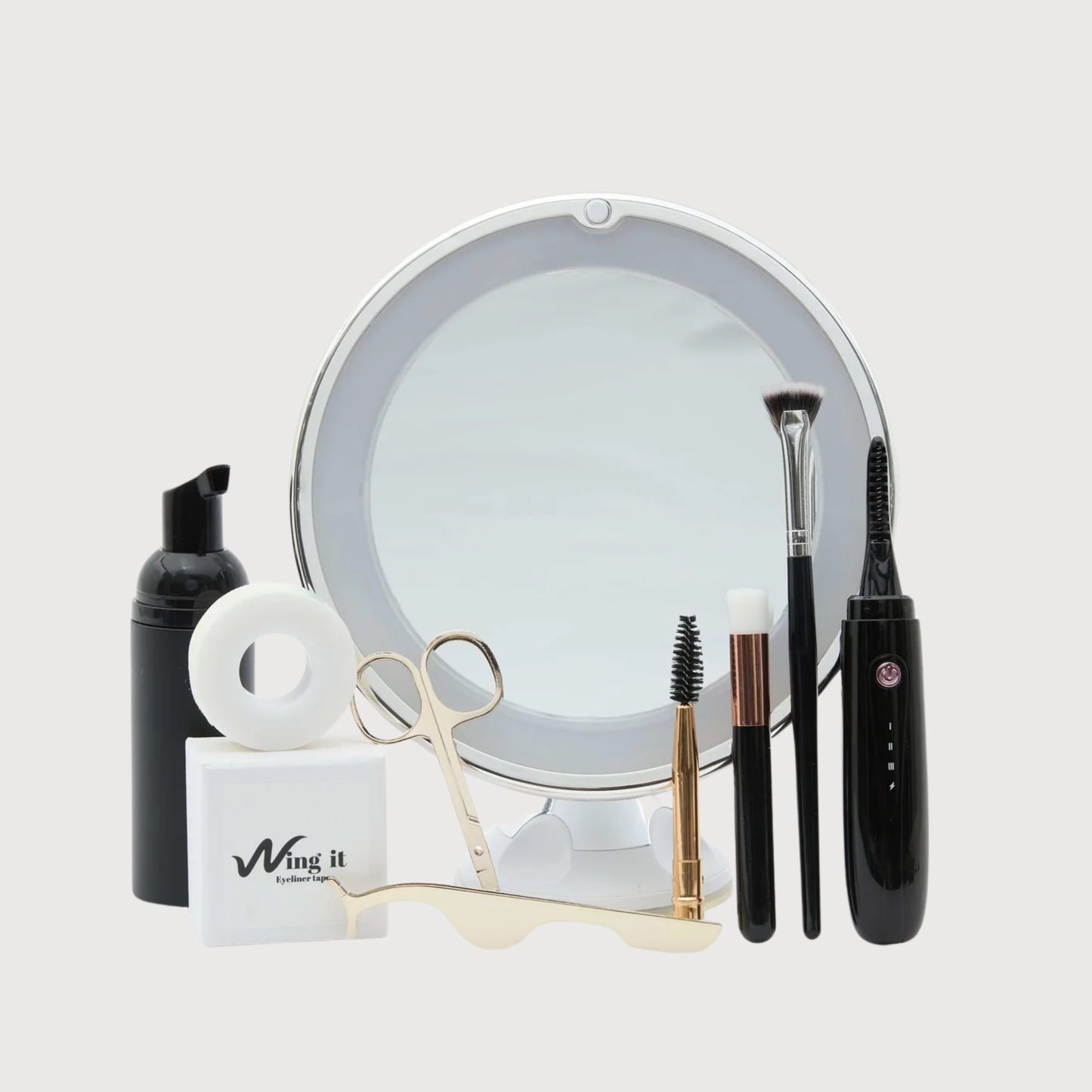 Collection of makeup and beauty tools including a mirror, brushes, and bottles on a light gray background.