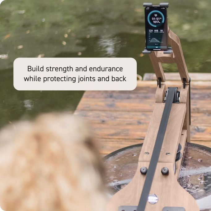 A wooden rowing machine on a dock with water in the background, featuring a smartphone mounted on the frame displaying workout metrics. A text overlay reads, 'Build strength and endurance while protecting joints and back.